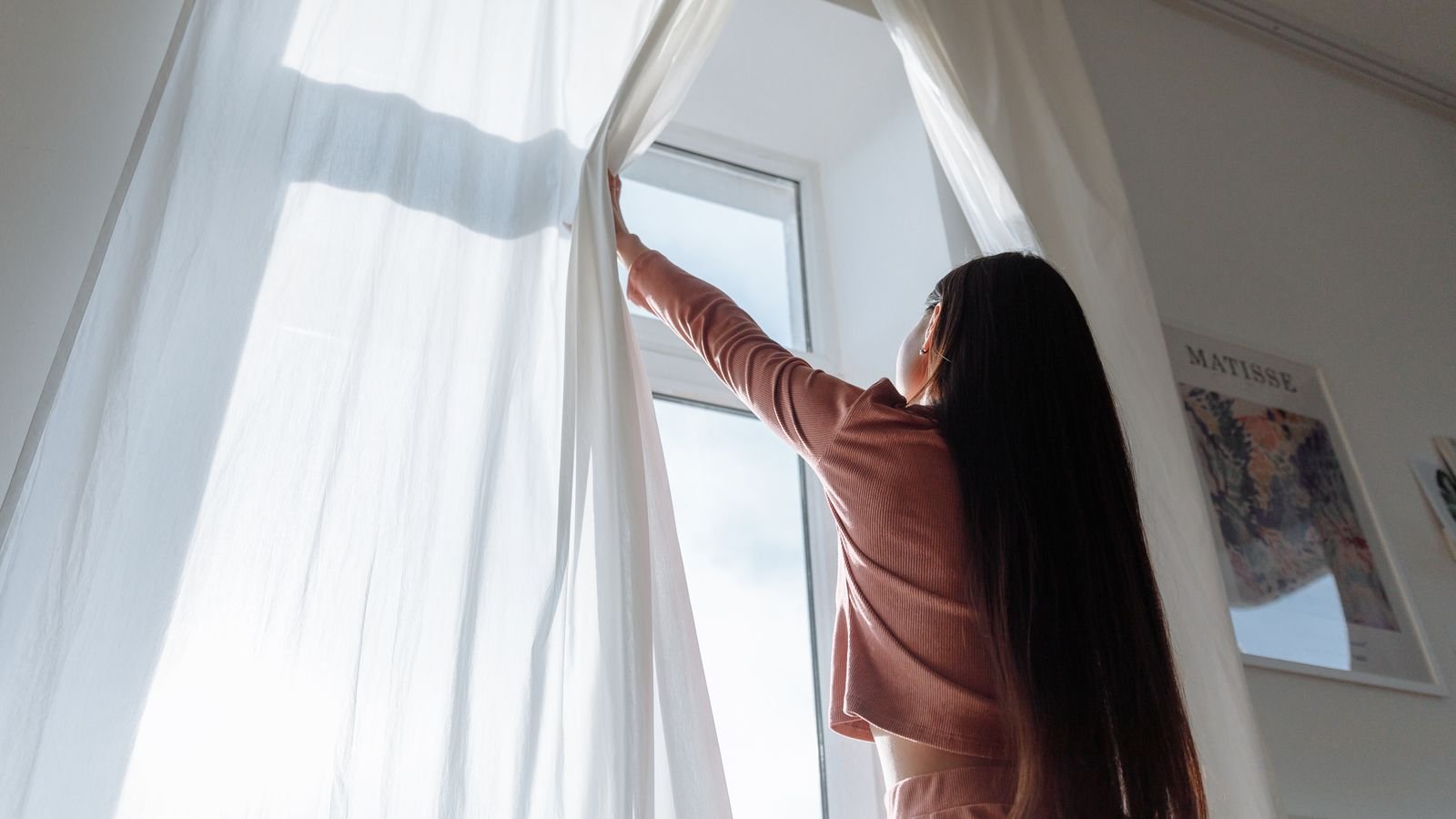 Woman opening white curtains in a bright living room