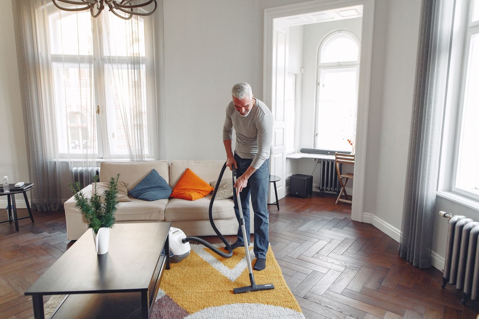 A man vacuuming a yellow rug in a bright living room