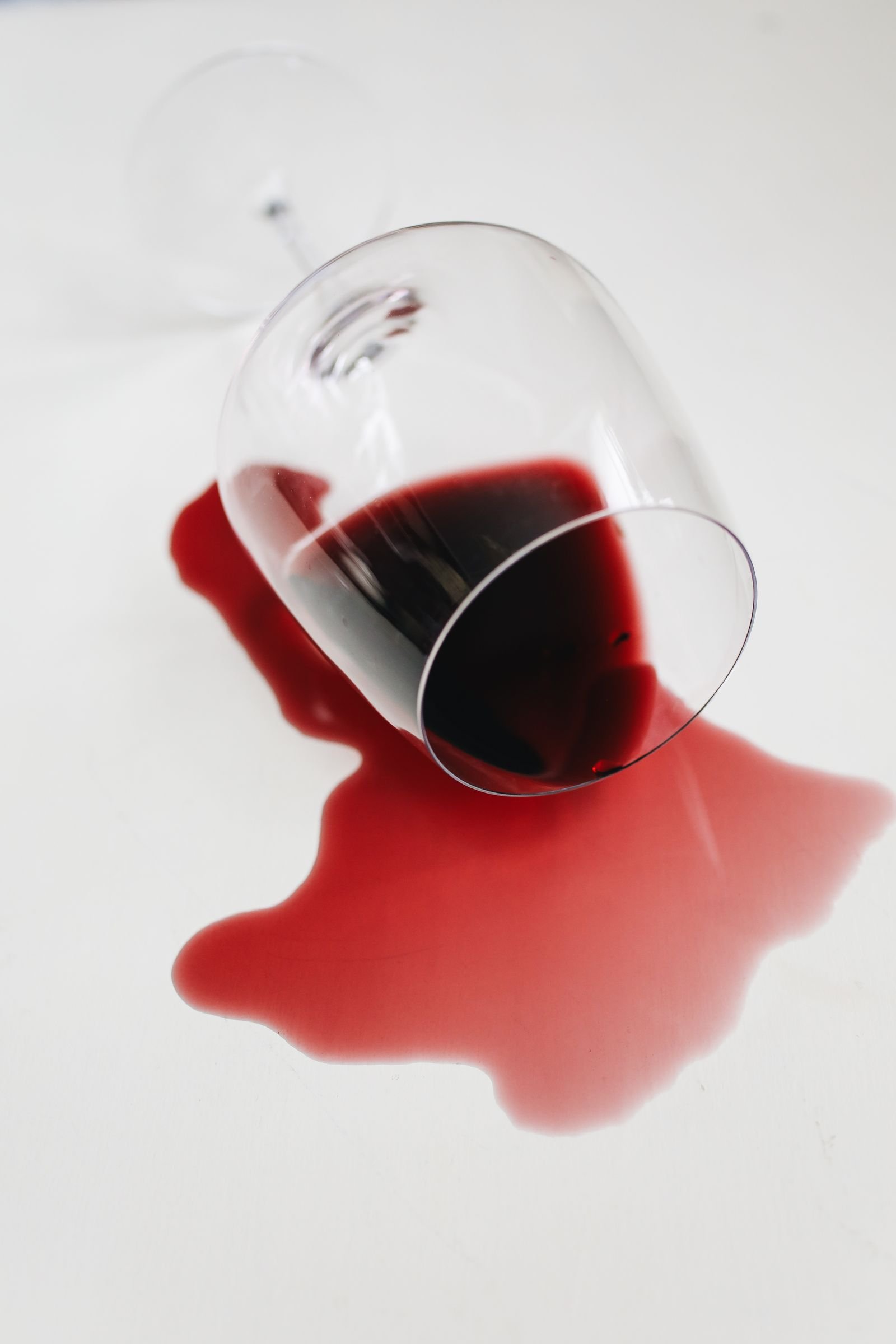 A tipped wine glass with red wine spilling across a pale floor