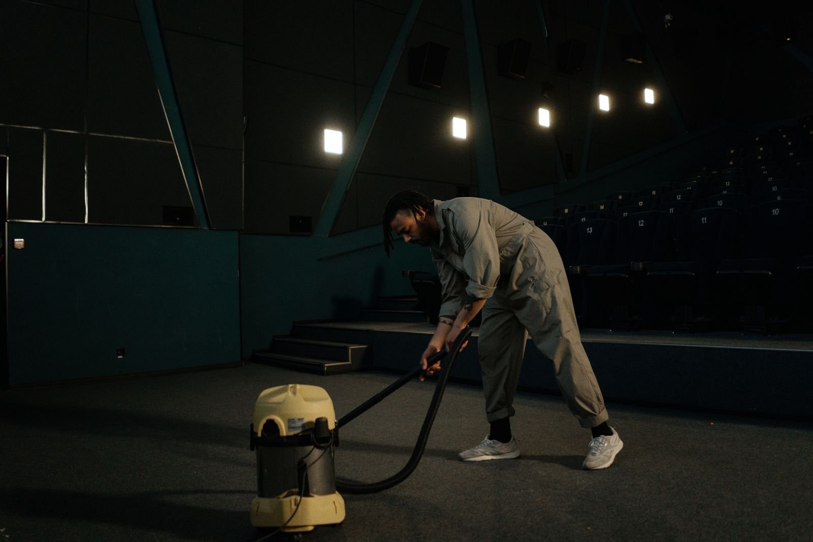 Encapsulation vs Hot Water Extraction for Commercial Carpet A cleaning operative in coveralls working a vacuum across a cinema carpet