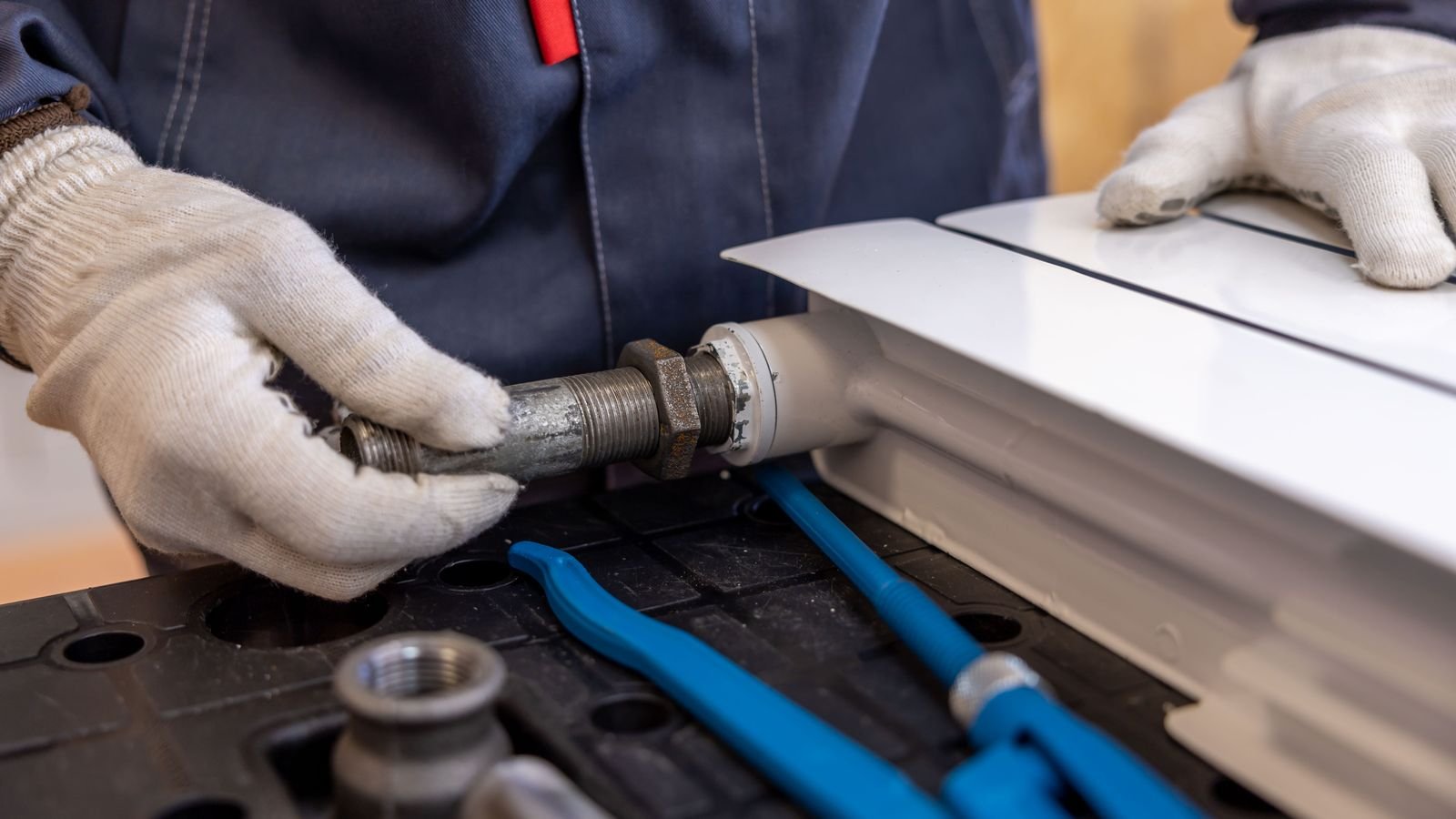 Plumber in gloves repairing a radiator pipe connection