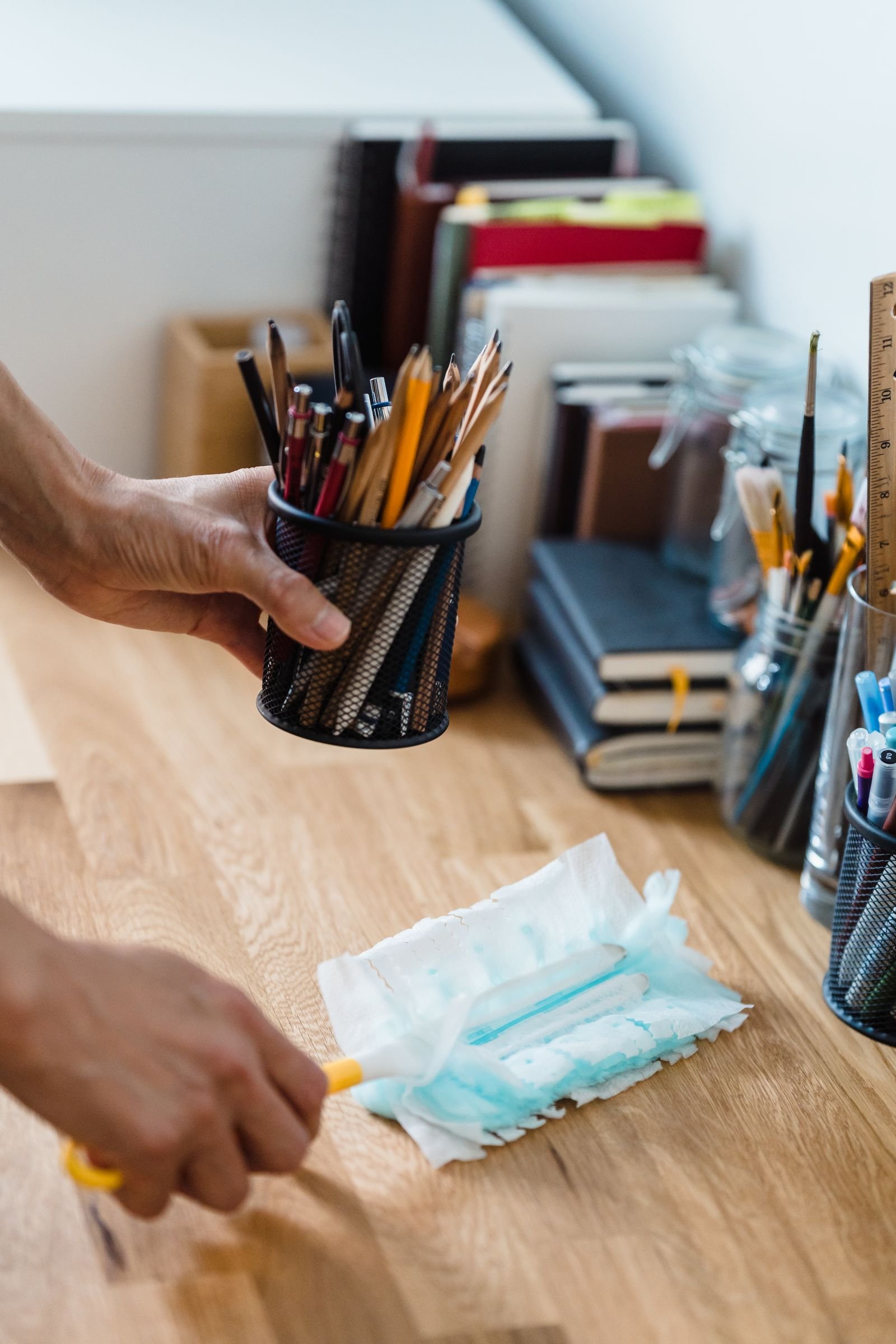 A hand dusting an office desk around stationery