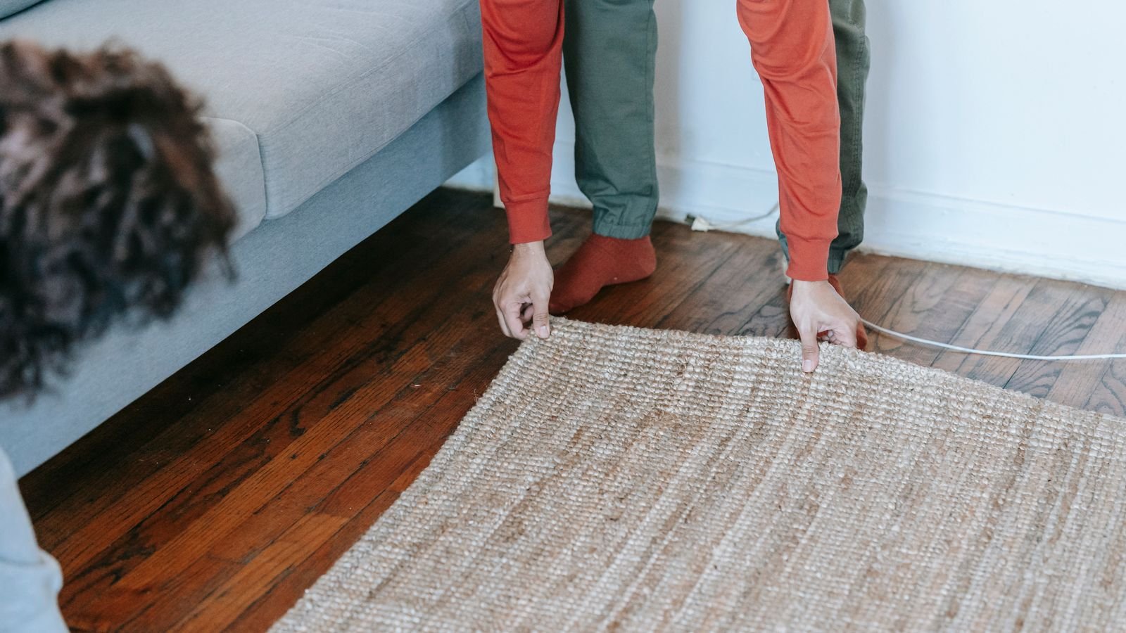 Two people lifting the corner of a rug from a wooden floor