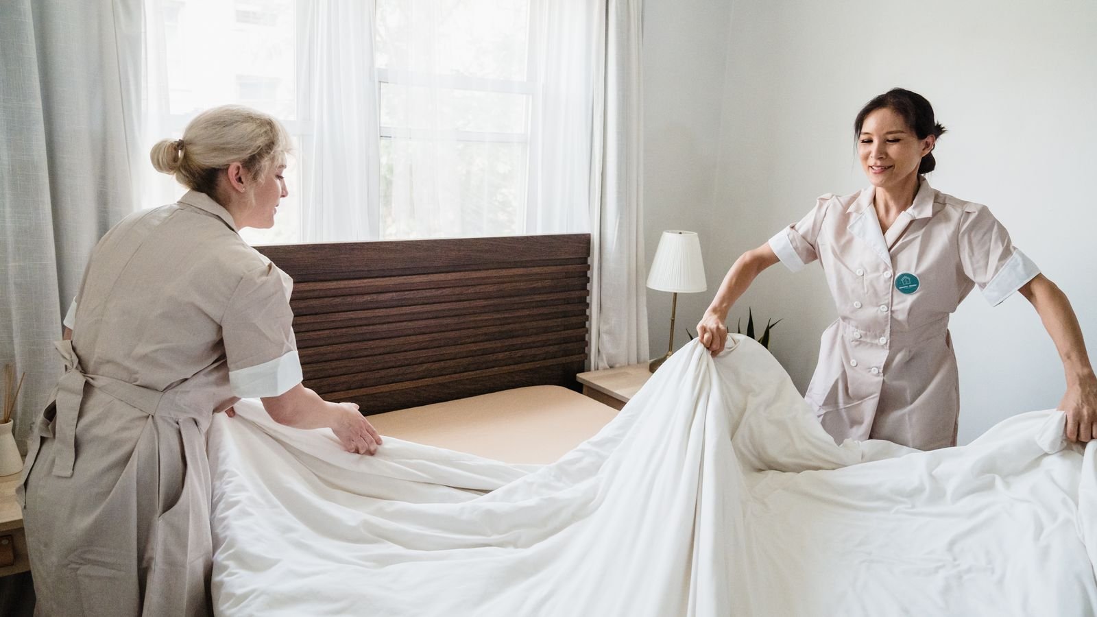 Two housekeepers making up a bed with fresh white linen