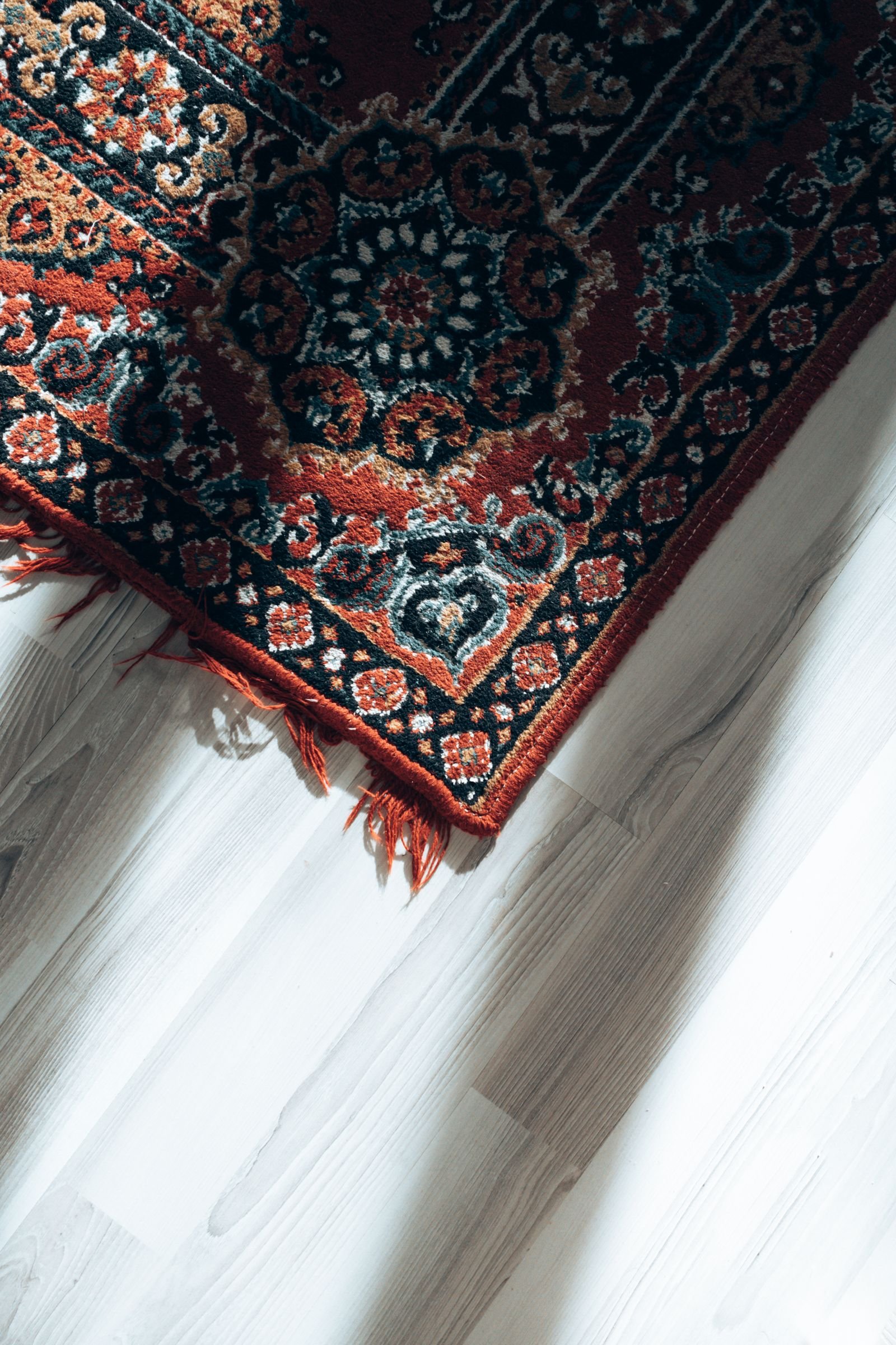 The fringed corner of a traditional wool rug on a pale wooden floor