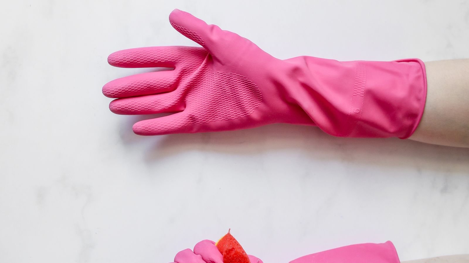 Hands wearing pink cleaning gloves beside a sponge Hands wearing pink cleaning gloves beside a sponge