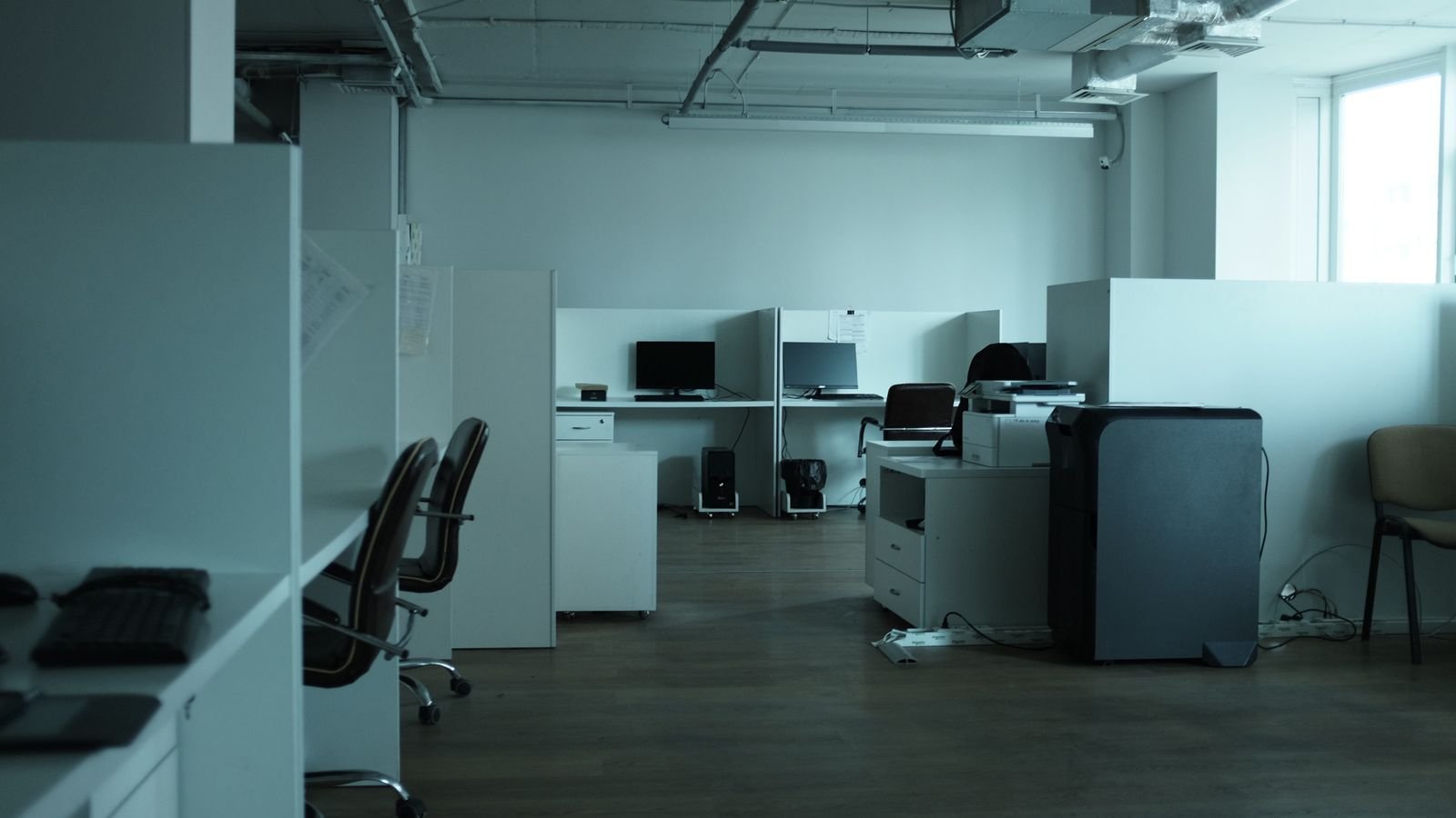 Empty open-plan office with desks, chairs and carpeted floor.