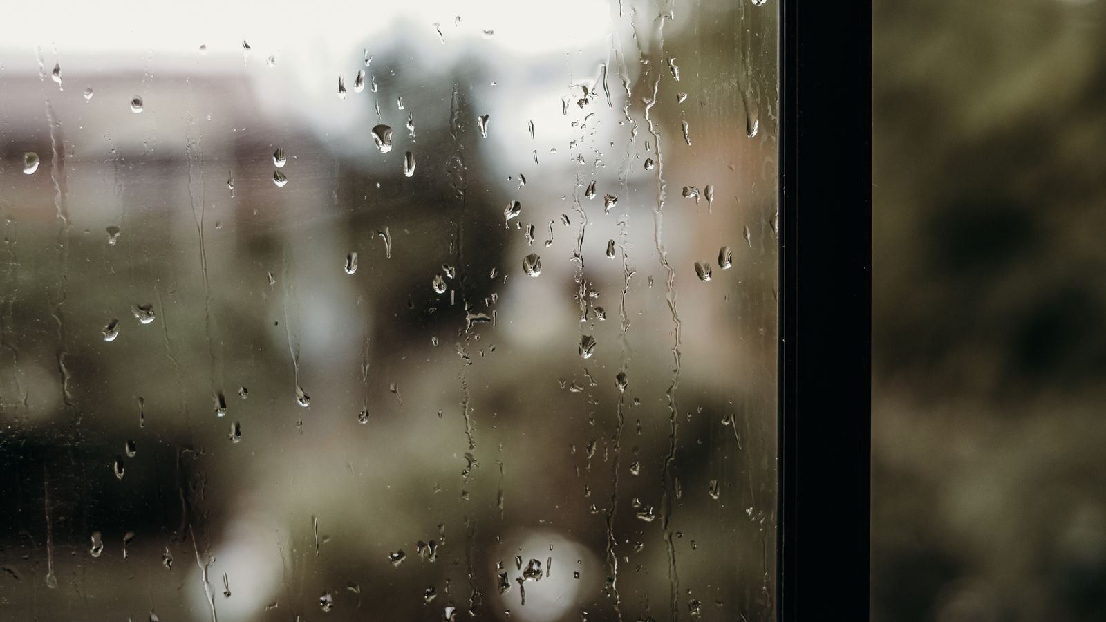 Raindrops running down a closed window pane with a blurred garden and house outside Raindrops running down a closed window pane with a blurred garden and house outside