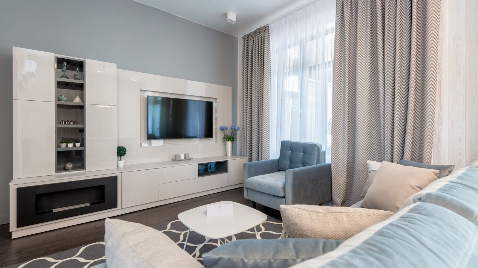 Bright modern living room with a sofa, cushions, armchair and fitted media unit.