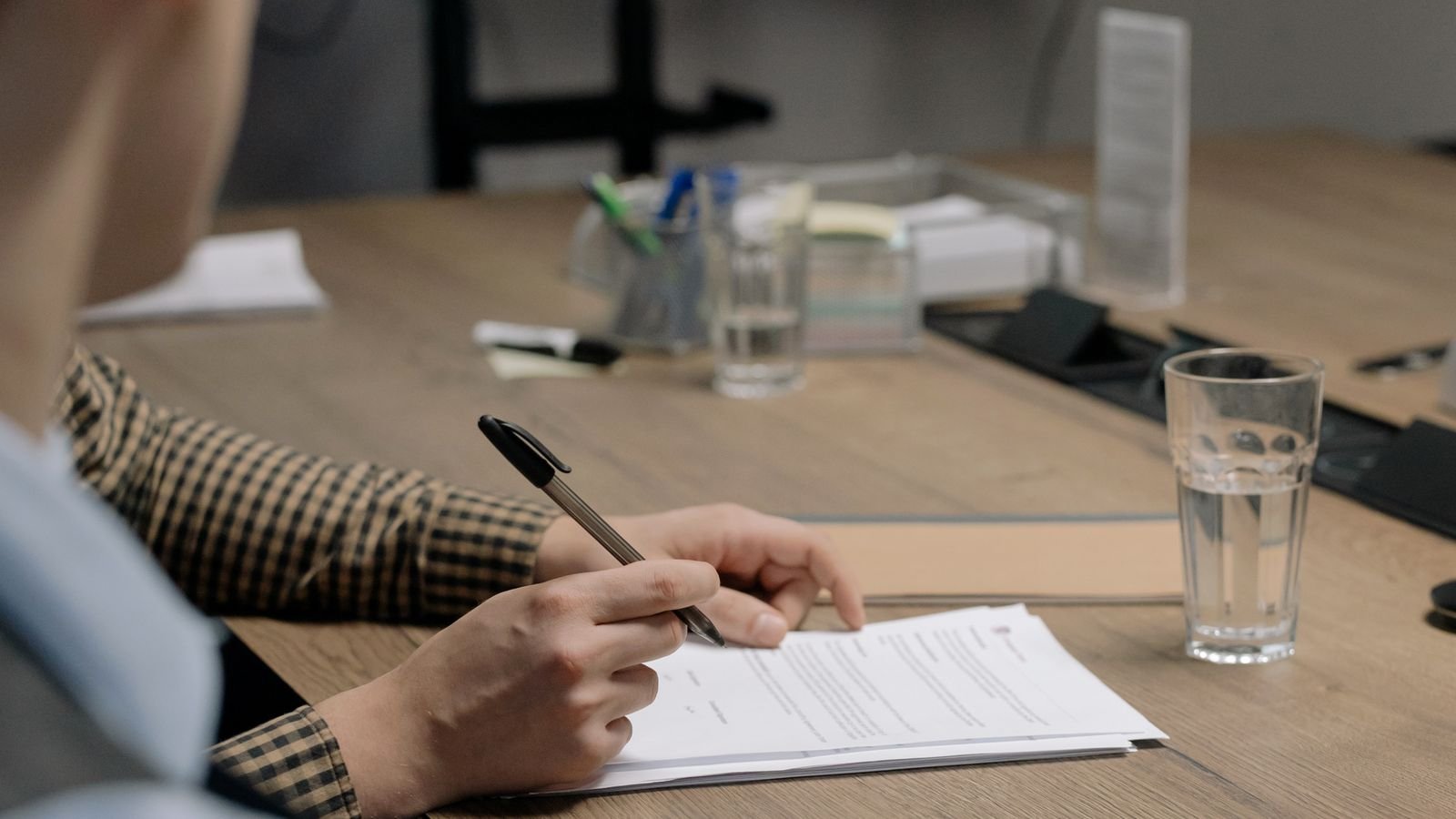 Person seated at a wooden office desk holding a pen over a printed document